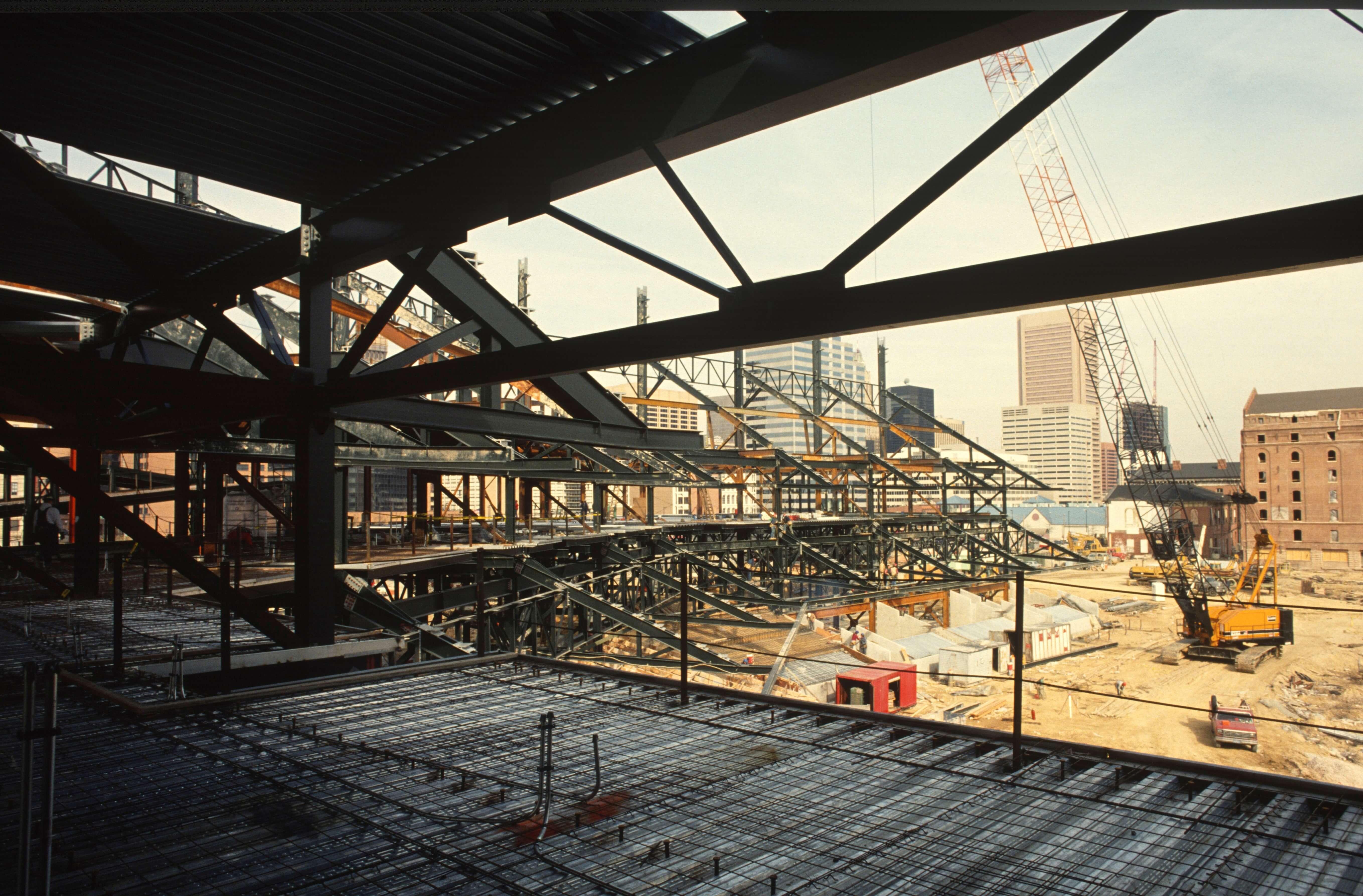Steel framework of Camden Yards under construction with downtown Baltimore skyline in the background.