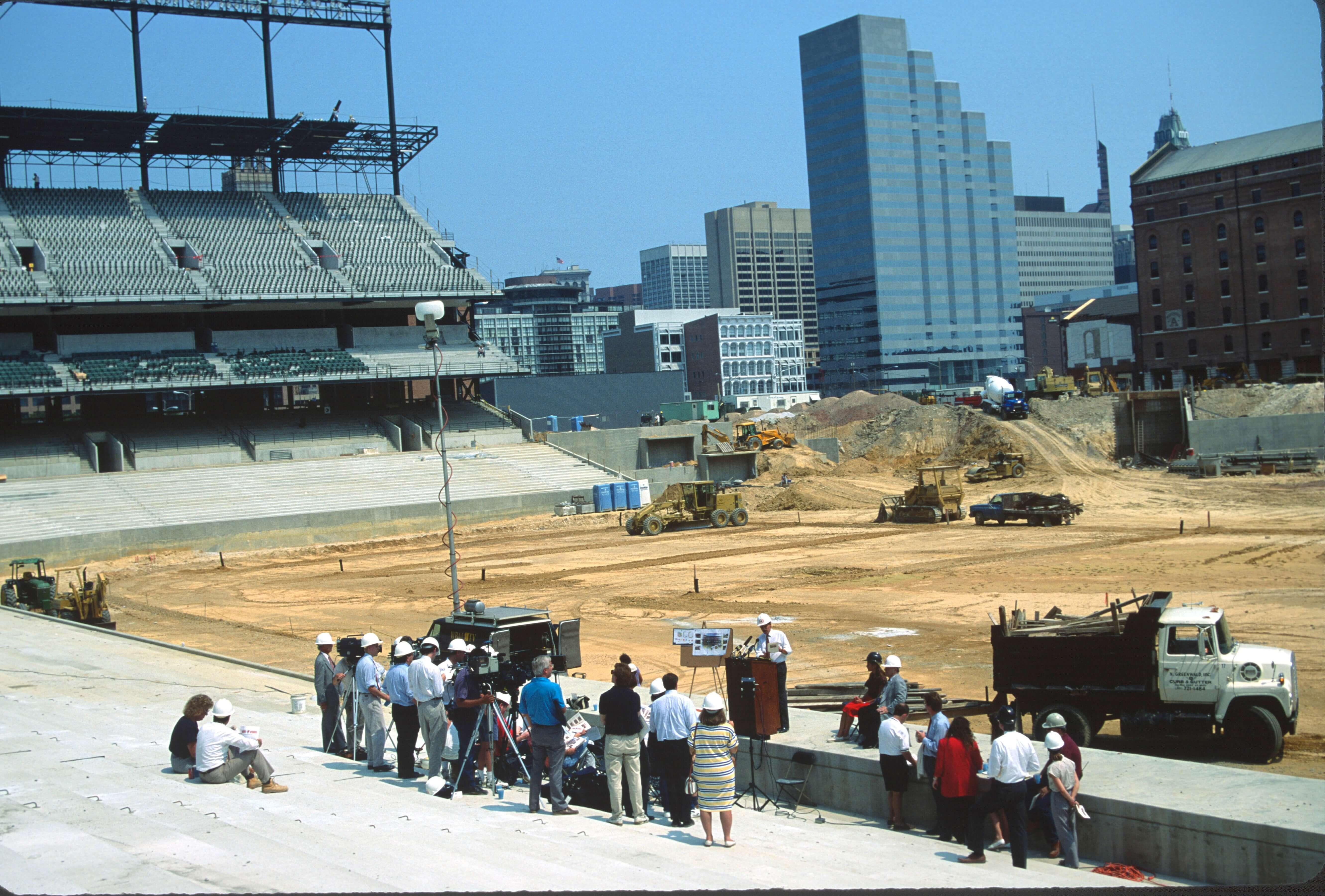 Interior view of the stadium construction site showing unfinished field area, seating sections, and heavy equipment.