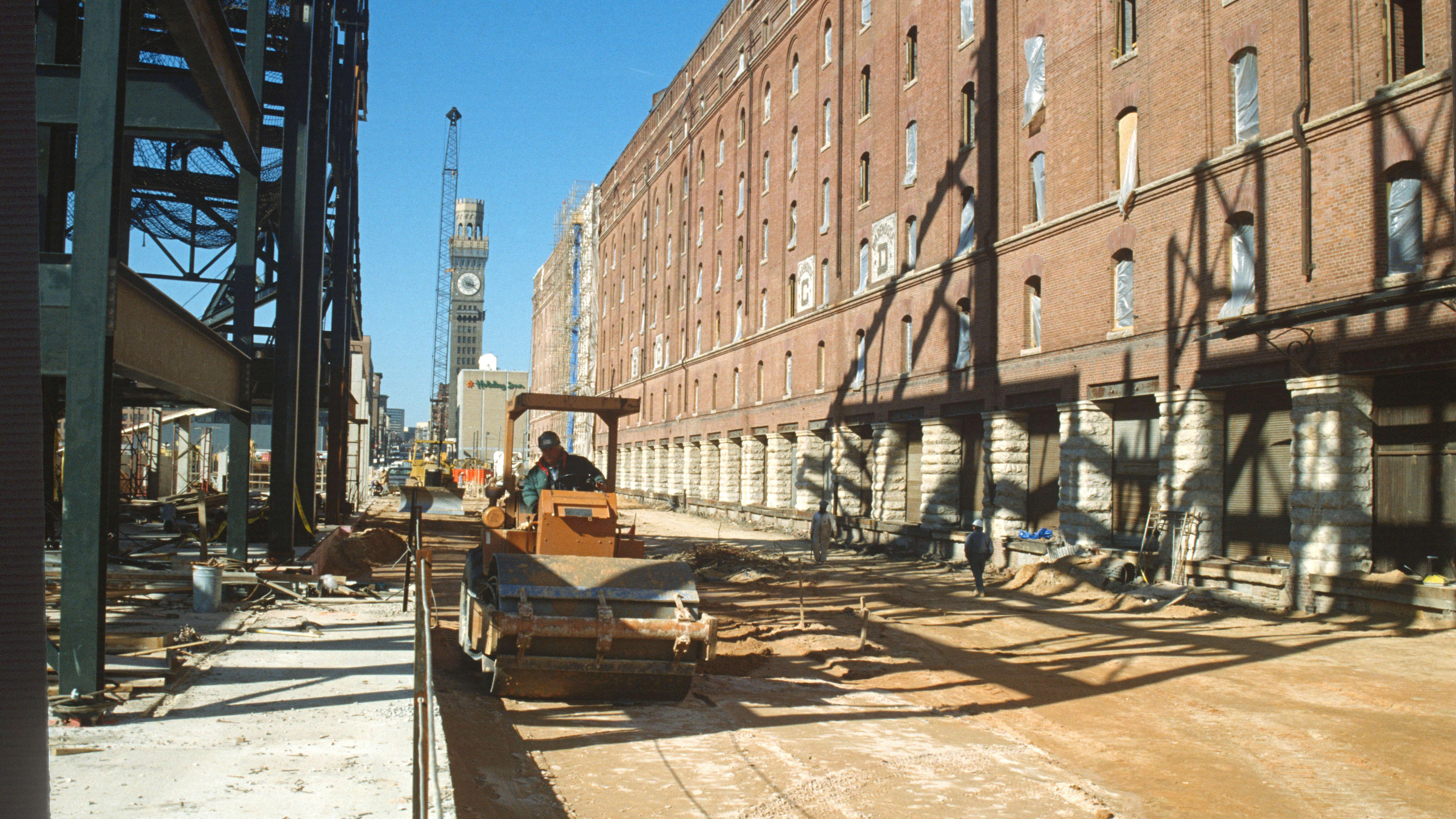 Steamroller paving ground alongside the brick warehouse during Camden Yards construction.