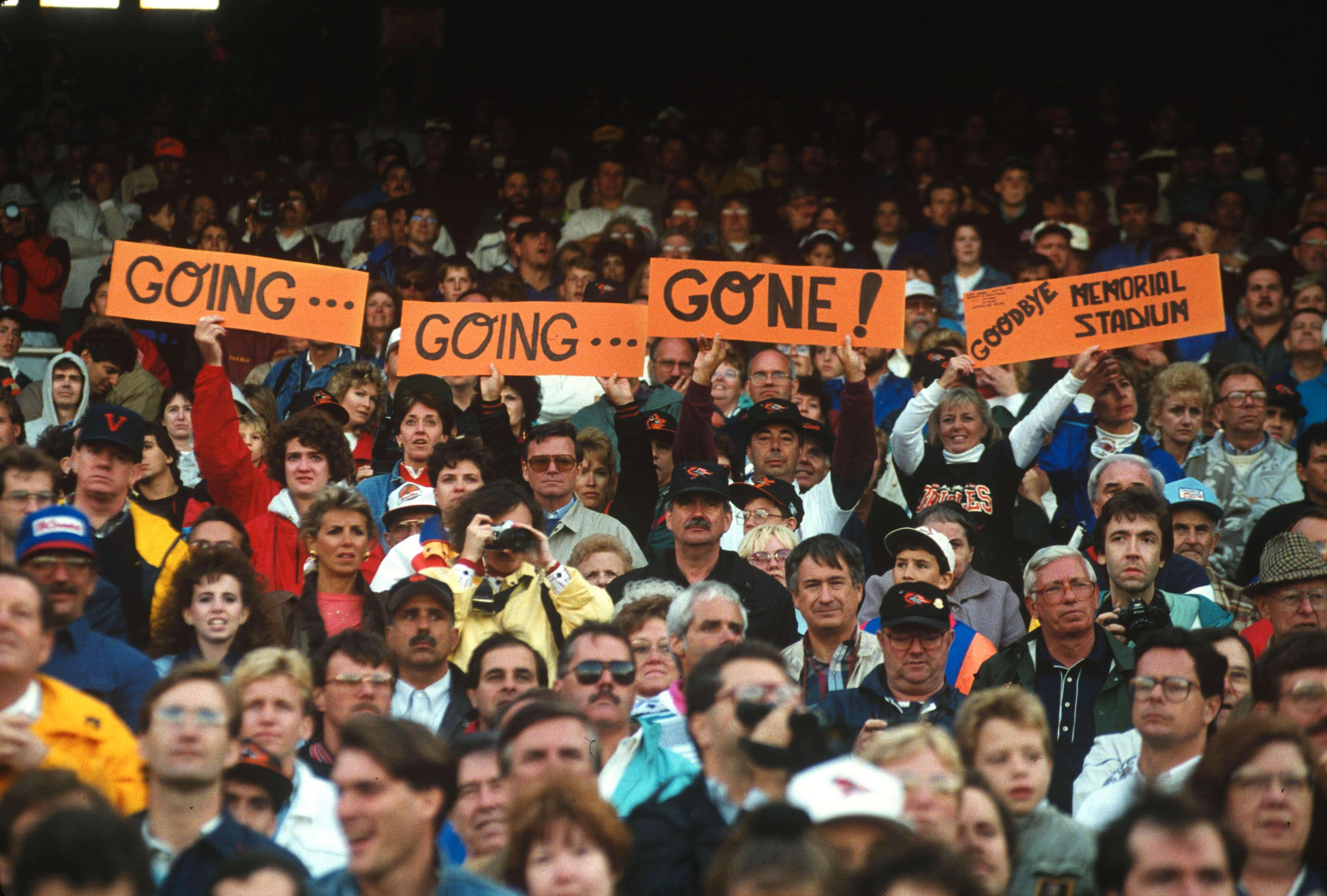 Fans hold orange signs reading “Going… Going… Gone!” and “Goodbye Memorial Stadium”