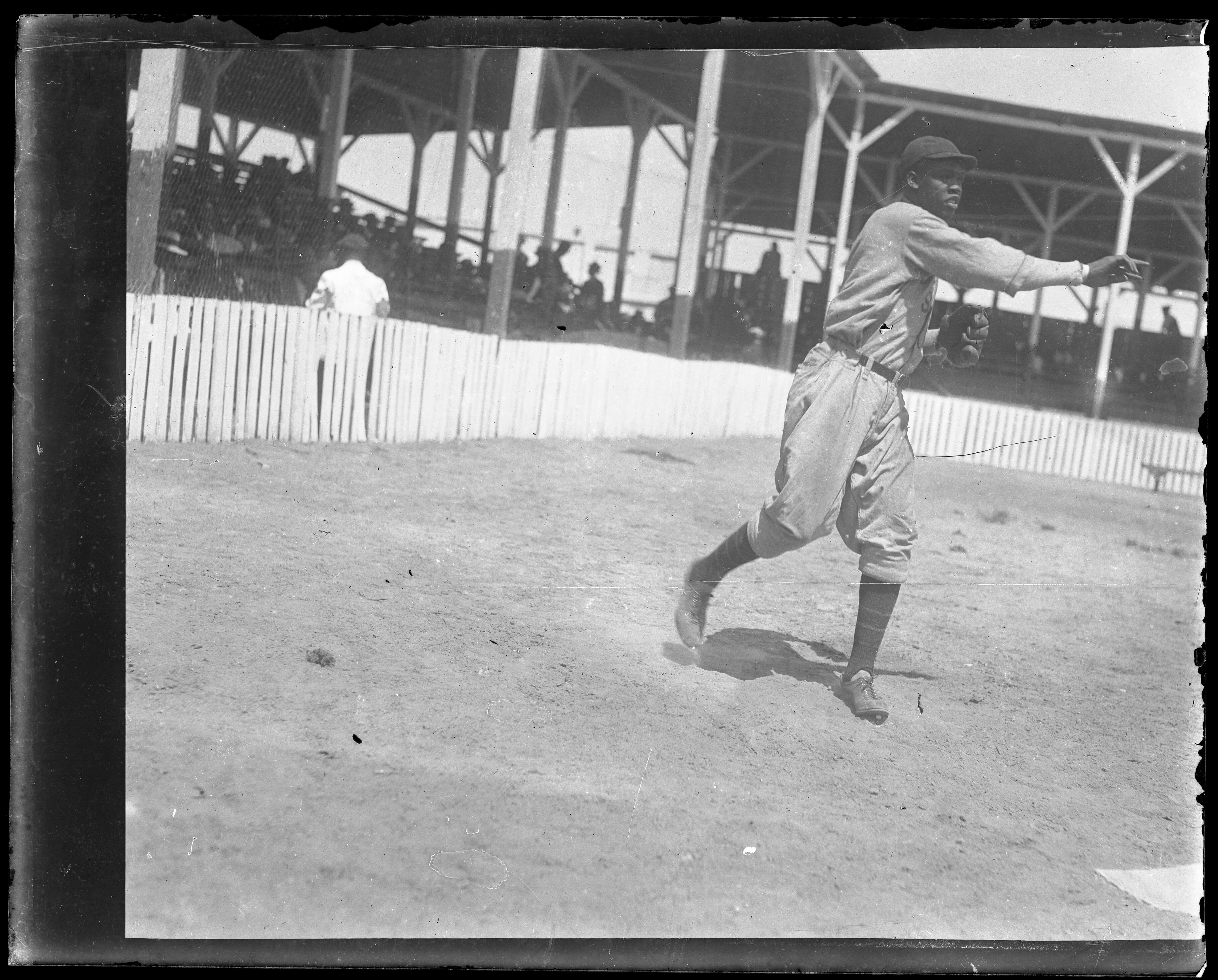 Laymon Samuel Yokely throwing a baseball on a field at Maryland Park stadium in 1929 with wooden grandstands behind him.