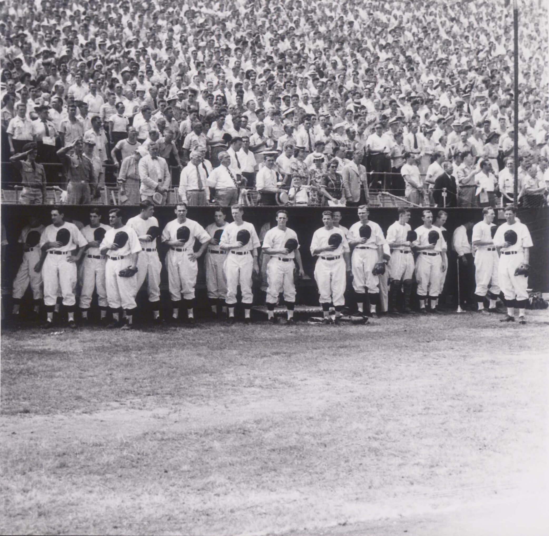 Players standing along the dugout before a game with a packed crowd behind them.