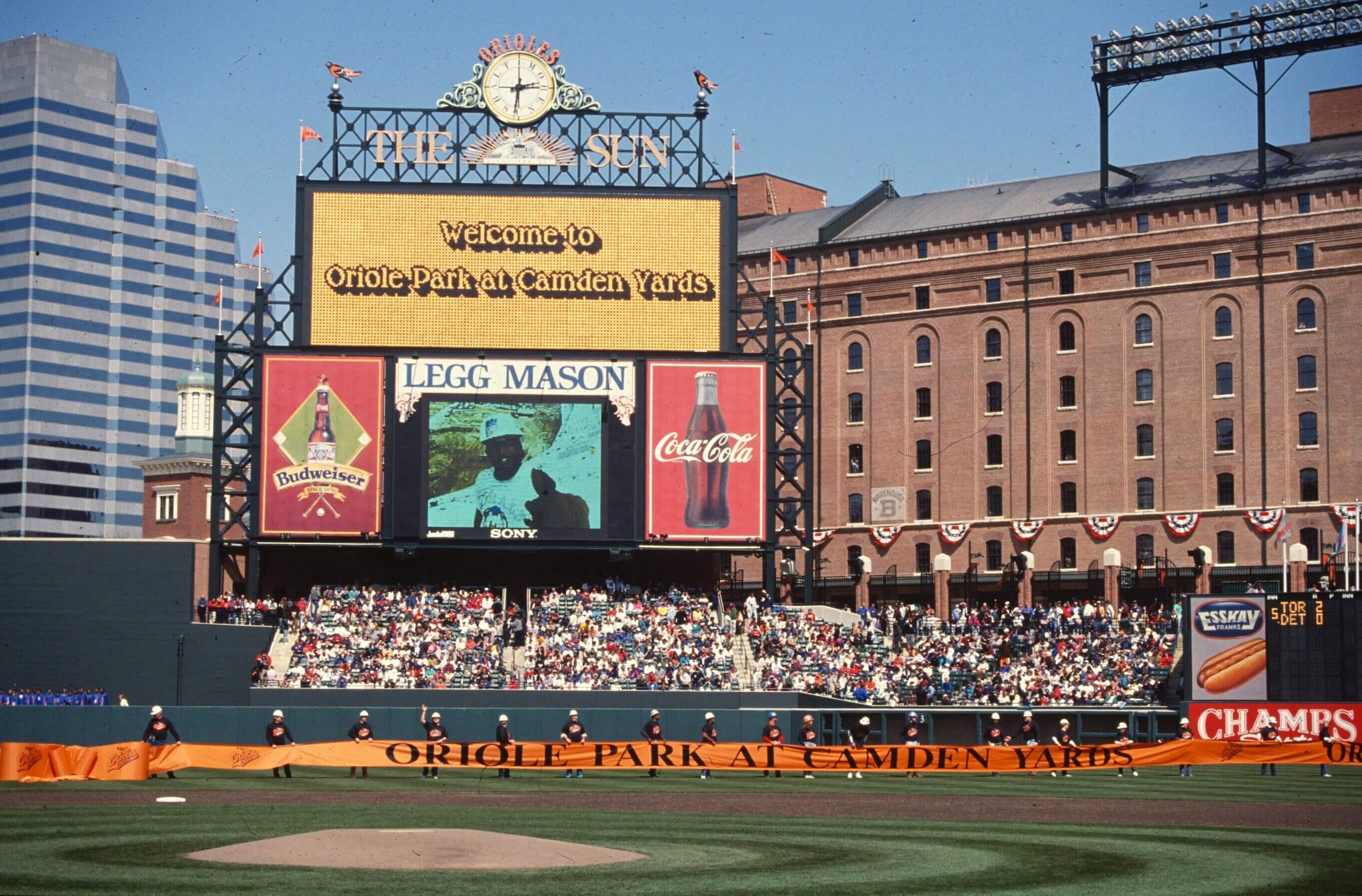 Stadium scoreboard displays “Welcome to Oriole Park at Camden Yards” as staff hold a long banner across the field during opening ceremonies.