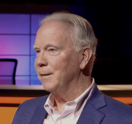 Smiling man wearing a blue suit in a colorful media room