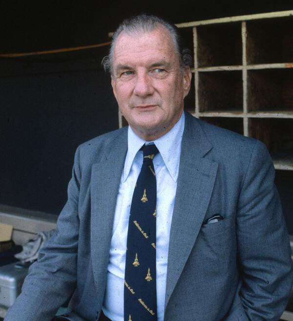 Portrait of a suited man standing inside a baseball dugout.