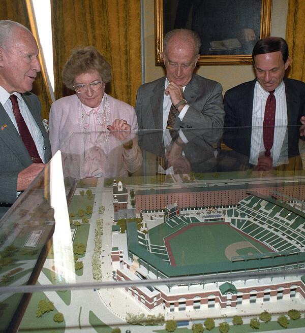 Officials and civic leaders examine a scale model of Oriole Park at Camden Yards inside a display case.